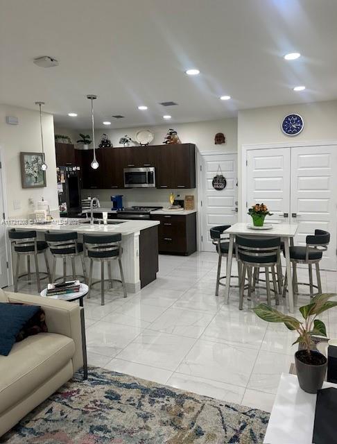 kitchen with a breakfast bar area, appliances with stainless steel finishes, hanging light fixtures, dark brown cabinetry, and sink