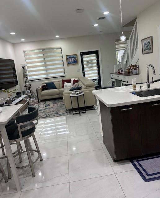 kitchen with decorative light fixtures, a kitchen island with sink, dark brown cabinetry, and sink