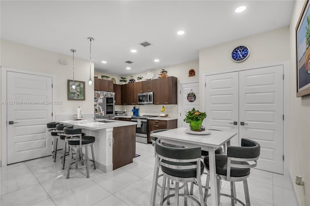 kitchen featuring pendant lighting, a breakfast bar area, light countertops, appliances with stainless steel finishes, and dark brown cabinetry