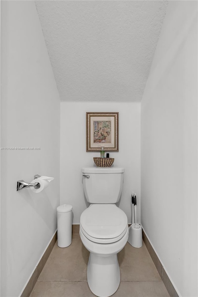 bathroom with a textured ceiling, tile patterned floors, toilet, and baseboards