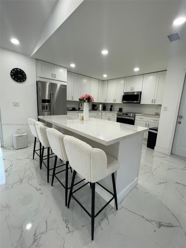 kitchen with white cabinets, stainless steel appliances, light stone countertops, and a large island