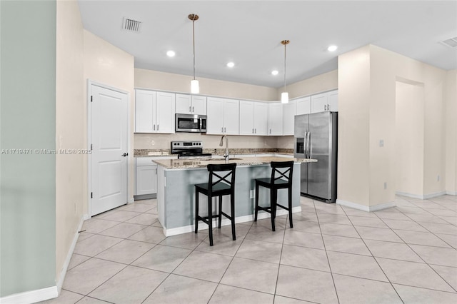 kitchen with light stone countertops, stainless steel appliances, white cabinetry, and a kitchen island with sink