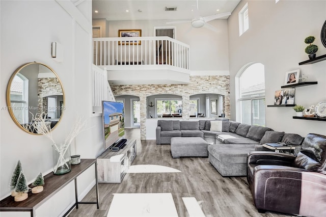 living room with ceiling fan, a towering ceiling, and light hardwood / wood-style flooring