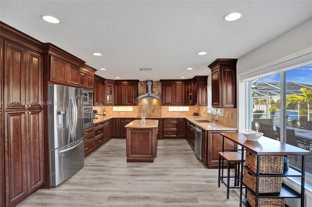 kitchen featuring appliances with stainless steel finishes, backsplash, dark brown cabinets, wall chimney range hood, and a kitchen island