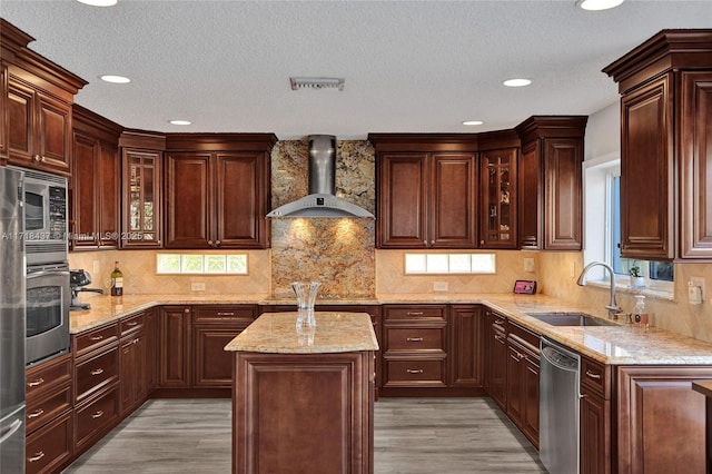 kitchen with a center island, sink, wall chimney exhaust hood, appliances with stainless steel finishes, and light wood-type flooring