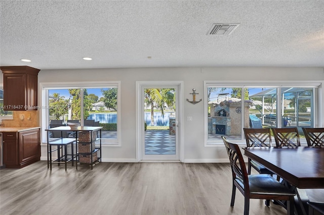 dining room with light wood-type flooring, a textured ceiling, a water view, and a wealth of natural light