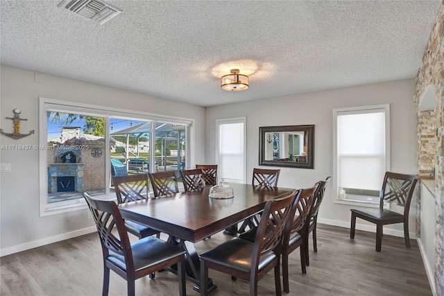 dining area with a stone fireplace, a textured ceiling, and hardwood / wood-style flooring