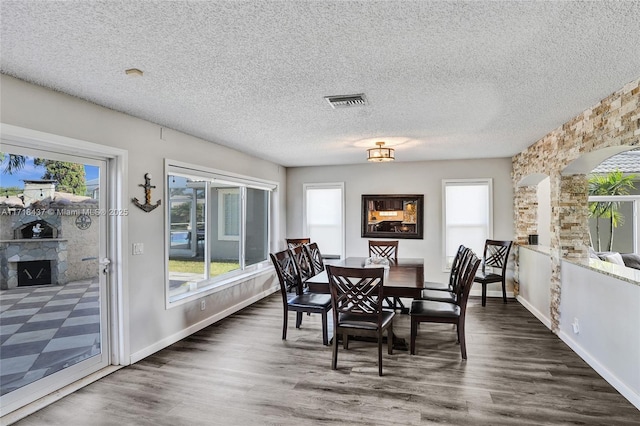 dining area with a textured ceiling, a stone fireplace, and dark wood-type flooring