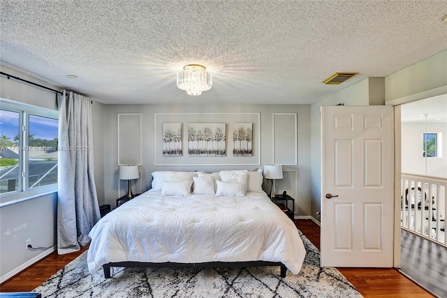 bedroom with hardwood / wood-style flooring, a textured ceiling, and a notable chandelier