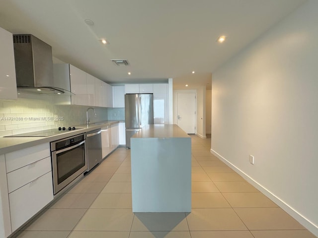 kitchen featuring sink, wall chimney exhaust hood, white cabinets, a kitchen island, and appliances with stainless steel finishes