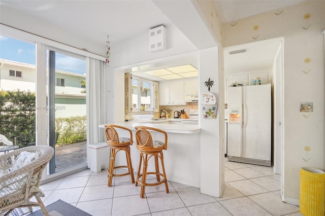 kitchen featuring white cabinets, kitchen peninsula, white appliances, a breakfast bar, and light tile patterned floors