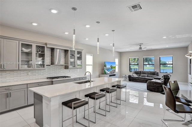 kitchen featuring gray cabinetry, ceiling fan, wall chimney range hood, and sink