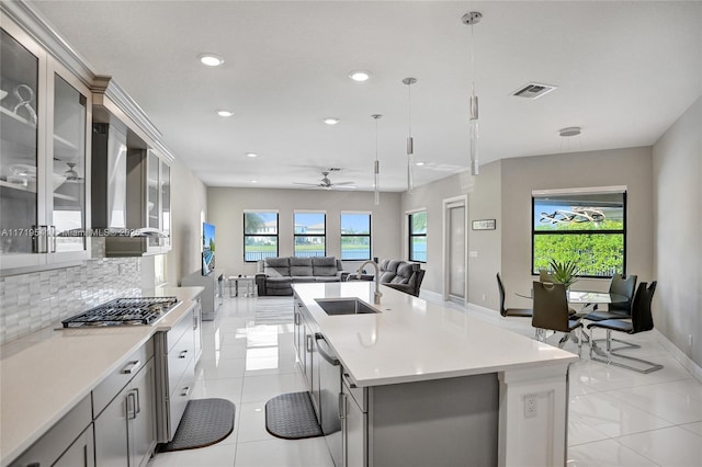 kitchen featuring ceiling fan, sink, tasteful backsplash, decorative light fixtures, and a center island with sink