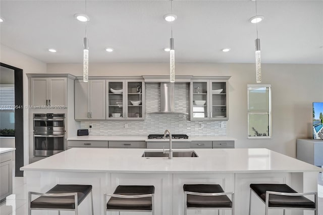 kitchen featuring wall chimney exhaust hood, hanging light fixtures, stainless steel double oven, a breakfast bar area, and gray cabinets