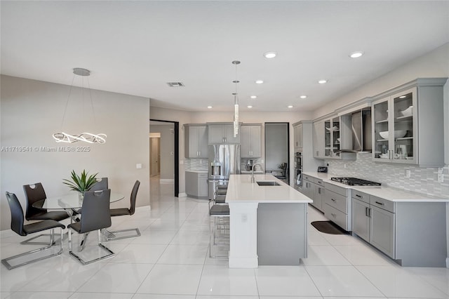 kitchen featuring a center island with sink, wall chimney range hood, sink, decorative light fixtures, and a breakfast bar area