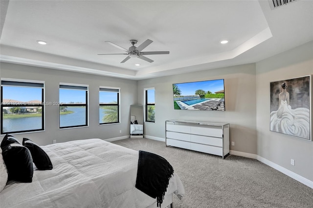 bedroom featuring ceiling fan, a raised ceiling, light colored carpet, and a water view