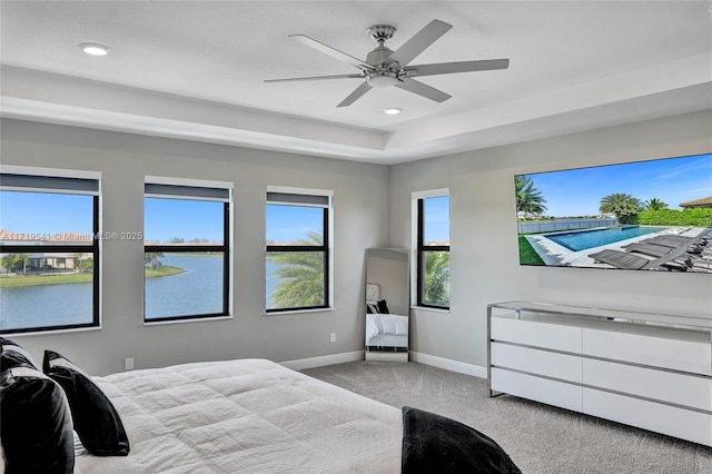 bedroom with a water view, ceiling fan, a tray ceiling, and light colored carpet