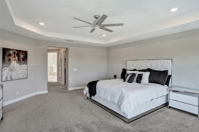 bedroom featuring ceiling fan, light colored carpet, ensuite bathroom, and a tray ceiling