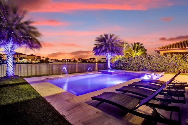 pool at dusk featuring pool water feature and an in ground hot tub