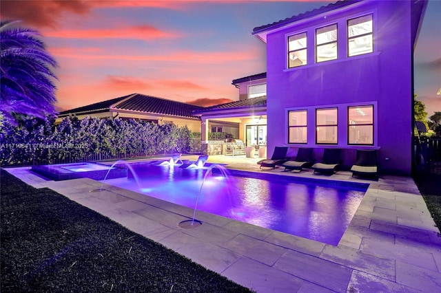 pool at dusk with a patio area, an in ground hot tub, and pool water feature