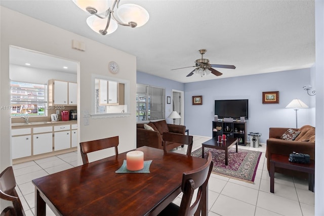 tiled dining area with a textured ceiling, sink, and ceiling fan with notable chandelier