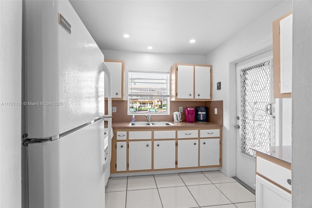 kitchen with white cabinetry, sink, light tile patterned floors, and white refrigerator