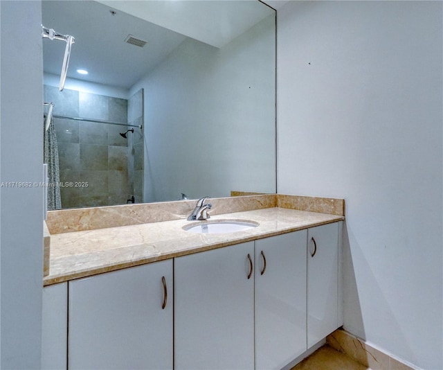 bathroom with visible vents, tiled shower, and vanity