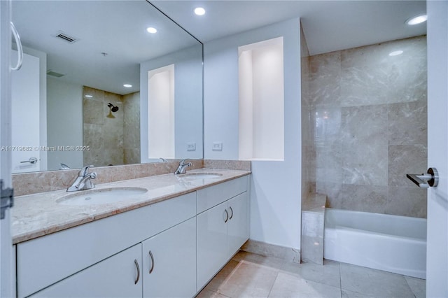 bathroom with baseboards, visible vents, tiled shower, and a sink