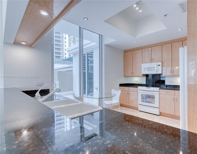 kitchen featuring recessed lighting, white appliances, light brown cabinets, and dark stone countertops