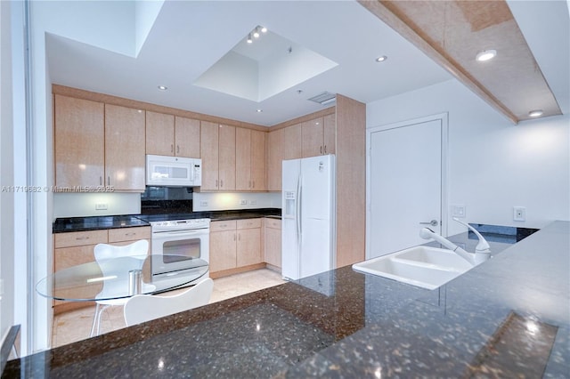 kitchen featuring recessed lighting, light brown cabinets, a sink, dark stone countertops, and white appliances