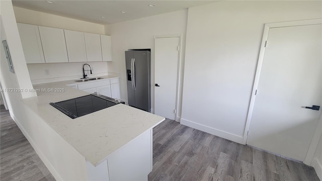 kitchen with white cabinetry, light wood-type flooring, stainless steel fridge with ice dispenser, and sink