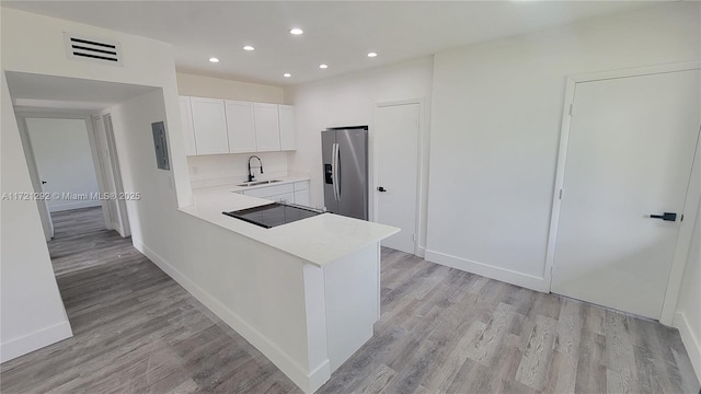 kitchen featuring sink, kitchen peninsula, stainless steel fridge, white cabinets, and light wood-type flooring