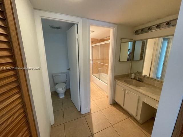 bathroom with a shower with shower door, toilet, vanity, and tile patterned flooring