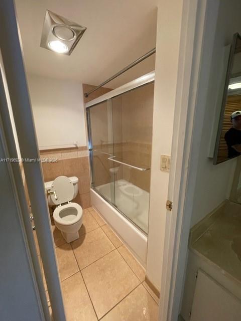 bathroom with tile patterned floors, toilet, and combined bath / shower with glass door