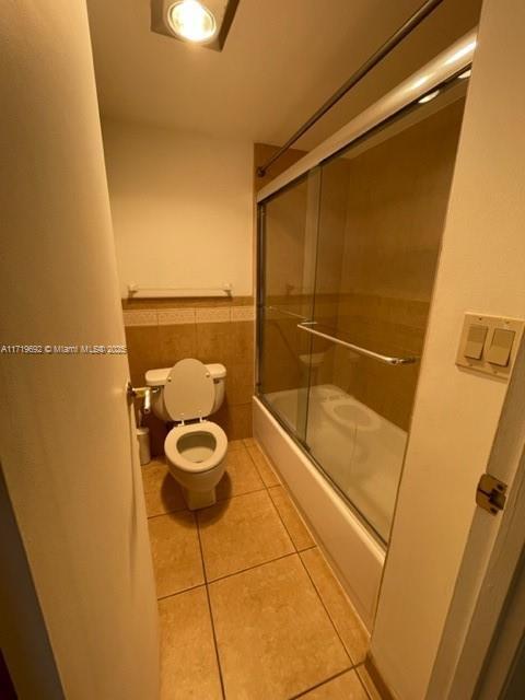 bathroom with toilet, combined bath / shower with glass door, tile patterned floors, and tile walls