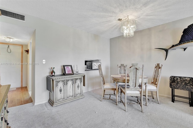 carpeted dining room featuring a textured ceiling and a chandelier