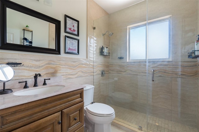 bathroom with a shower with door, vanity, tile walls, and toilet