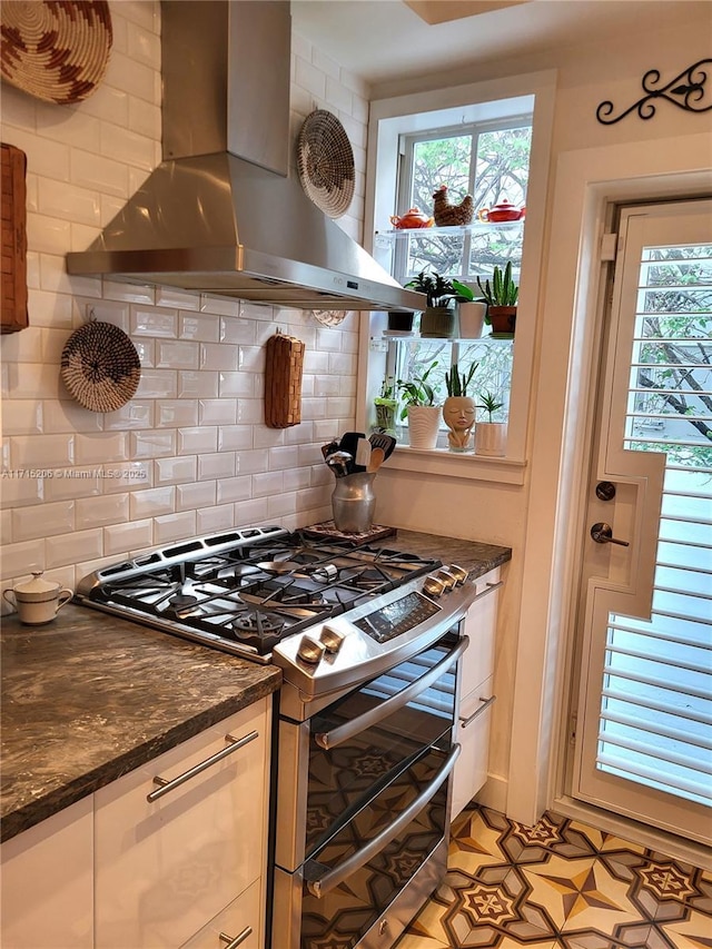 kitchen with stainless steel gas stove, backsplash, dark stone countertops, and wall chimney range hood