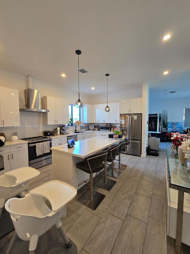 kitchen featuring white cabinetry, wall chimney range hood, hanging light fixtures, and appliances with stainless steel finishes