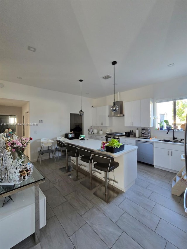 kitchen with pendant lighting, white cabinets, wall chimney range hood, sink, and appliances with stainless steel finishes