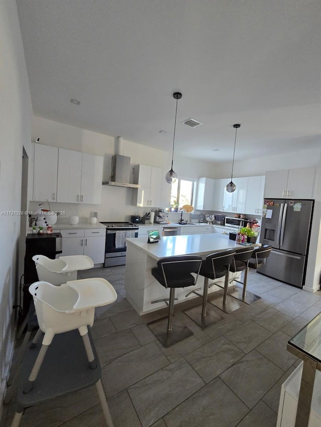 kitchen featuring a center island, wall chimney exhaust hood, appliances with stainless steel finishes, decorative light fixtures, and white cabinetry