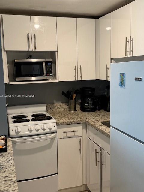 kitchen with white cabinets, white appliances, and light stone countertops