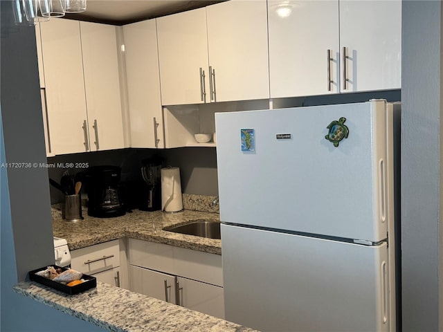 kitchen featuring sink, white fridge, white cabinetry, and light stone counters