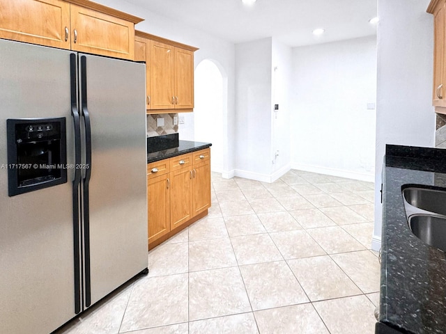 kitchen with dark stone countertops, stainless steel fridge with ice dispenser, light tile patterned floors, and tasteful backsplash