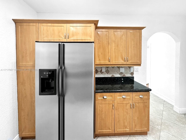 kitchen featuring decorative backsplash, dark stone countertops, light tile patterned floors, and stainless steel refrigerator with ice dispenser