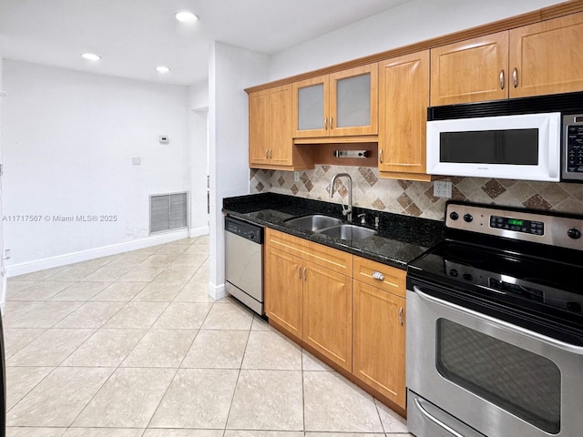 kitchen featuring sink, stainless steel appliances, tasteful backsplash, dark stone countertops, and light tile patterned floors