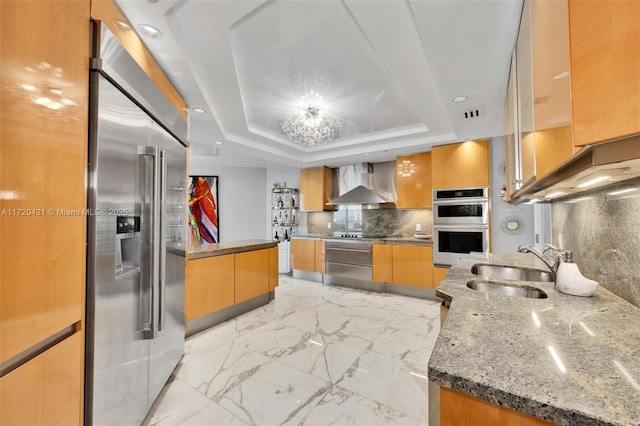 kitchen featuring wall chimney exhaust hood, sink, a kitchen island, decorative backsplash, and stainless steel appliances