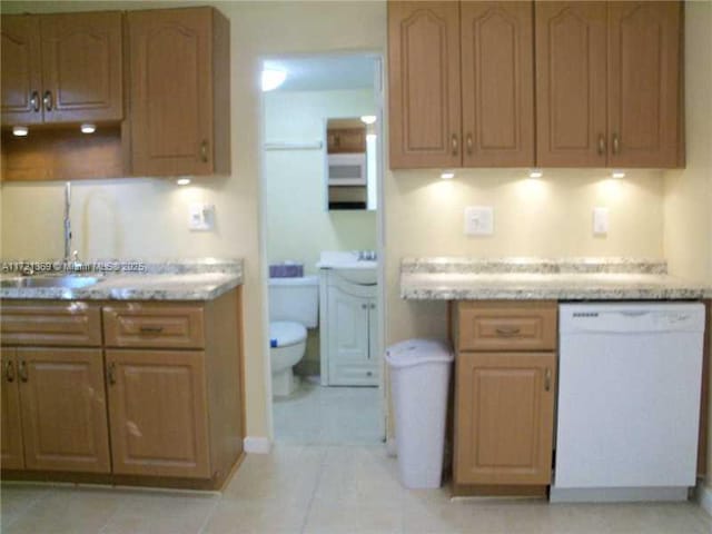 kitchen featuring white dishwasher, light stone countertops, light tile patterned floors, and sink