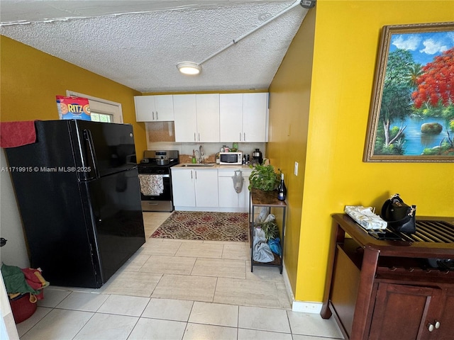 kitchen featuring black refrigerator, a textured ceiling, stainless steel range oven, white cabinets, and sink