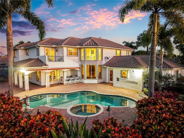 back of property at dusk with a patio, a tile roof, a balcony, and stucco siding